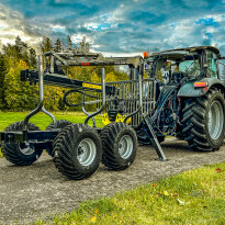 Czarna przyczepa leśna z hydraulicznym żurawiem HDS podłączona do ciągnika rolniczego na tle nieba
