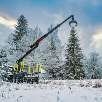Żuraw hydrauliczny z chwytakiem zamontowany na przyczepie leśnej podczas pracy w zimowym lesie przy załadunku drewna