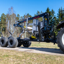 Czarna przyczepa leśna z żurawiem hydraulicznym i chwytakiem do drewna na tle lasu, słoneczny dzień
